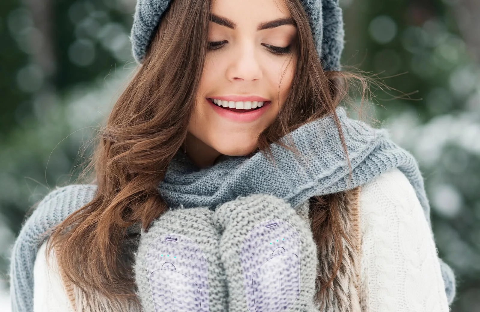 A woman in a knit hat and gray scarf holding two purple UNIHAND hand warmers inside her mittens